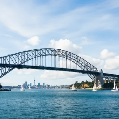 The iconic Auckland Harbour Bridge arching over the Waitematā Harbour, with the Auckland city skyline and Sky Tower visible in the background under a clear blue sky.